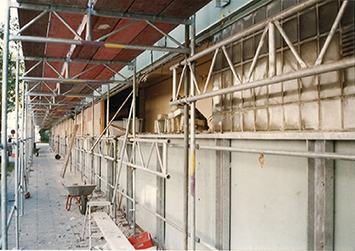 Blick auf die Fassade des Jugendhauses Düsseldorf während der Sanierung 1997. Sichtbare Gerüste, Werkzeuge wie eine Schubkarre und Material auf dem Boden.