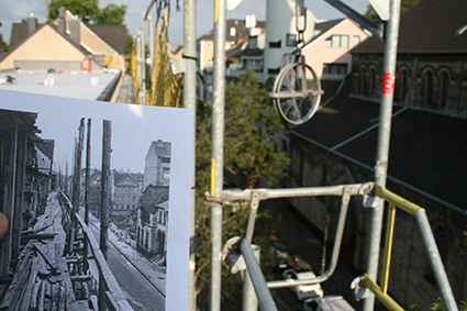 Blick von einem Gerüst auf eine Baustelle in Düsseldorf, im Vordergrund ein Foto einer historischen Ansicht der gleichen Straße. Sichtbare Gebäude und Gerüstteile.