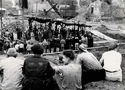 Eine Gruppe von Menschen beobachtet gespannt die Grundsteinlegung des Jugendhauses Düsseldorf auf einer historischen Aufnahme.